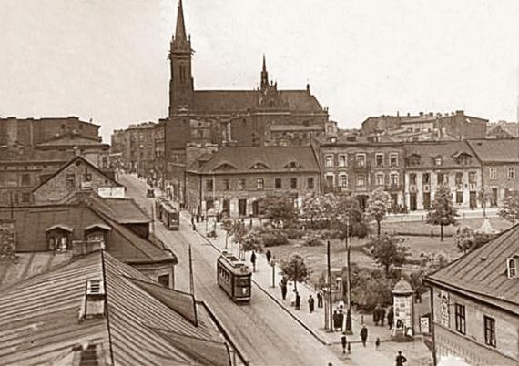 Historischer Straßenzug mit Häusern, rechts ein Platz mit Kirche im Hintergrund