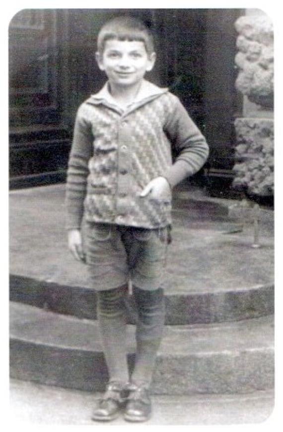 A boy standing in front of a doorstep, one hand in his jacket pocket, smiling at the camera