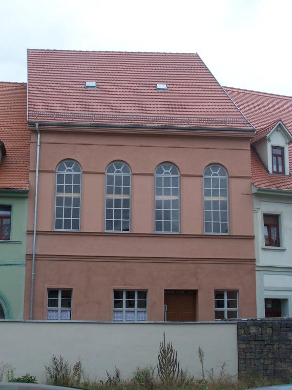 Reddish plastered building with four large arched windows on the upper floor.