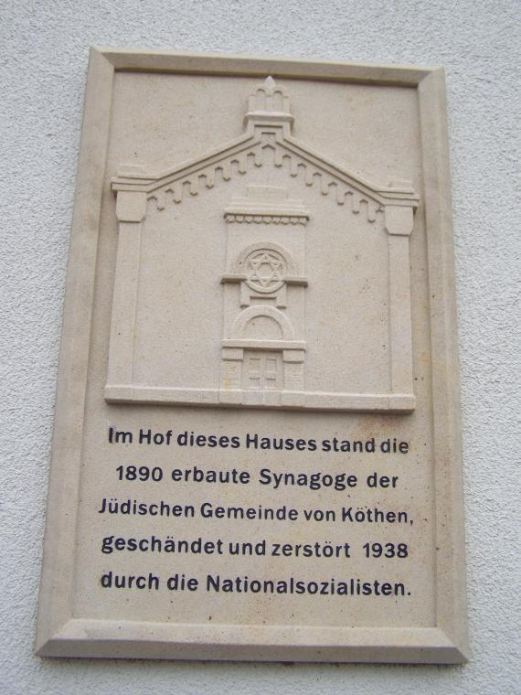 Gedenktafel mit einer Ansicht der Synagoge als Relief und dem Text: "Im Hof dieses Hauses stand die 1890 erbaute Synagoge der Jüdischen Gemeinde von Köthen, geschändet und zerstört 1938 durch die Nationalsozialisten".