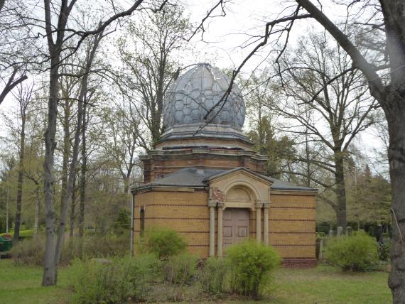 Yellowish brick building with dome. In front of the octagonal central building is a rectangular building with a columned portal.