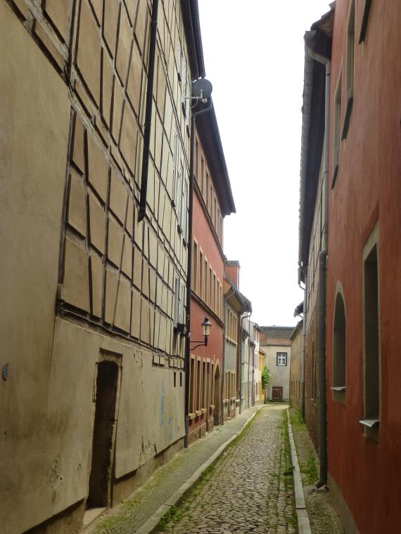 Eine schmale Gasse mit Gehwegen auf beiden Seiten und Häusern verschiedener Stilepochen, darunter Fachwerkbauten, mit unterschiedlichen Gebäudehöhen.