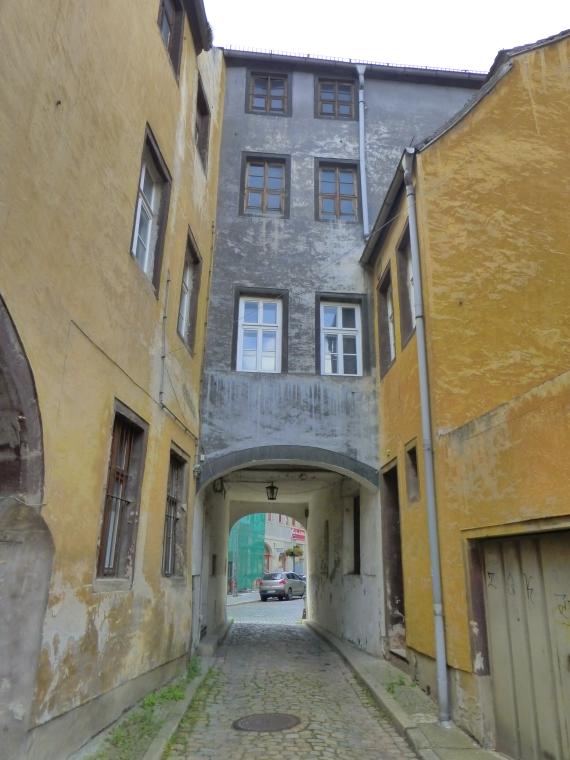 A narrow alleyway leads through a double archway, above which there are three storeys of a house.