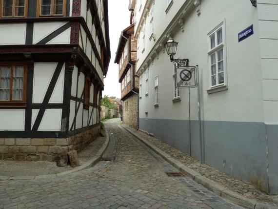 Eingang in eine schmale Gasse mit mehrgeschossigen Fachwerkhäusern links und rechts. Im Hintergrund eine Mauer im weiteren Verlauf der Gasse. 