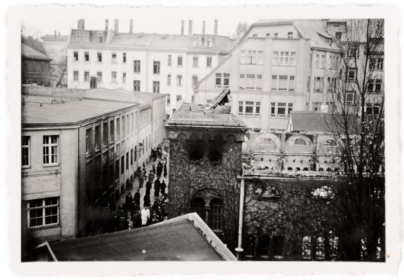 Schwarz-weiß Fotografie aus erhöhter Perspektive auf eine ausgebrannte Ruine einer ehemaligen Synagoge mit angrenzenden Wohnhäusern