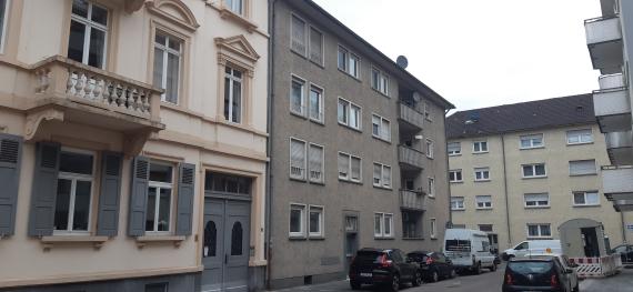 Foto einer Straße mit Häusern verschiedener Baustile und parkende Autos