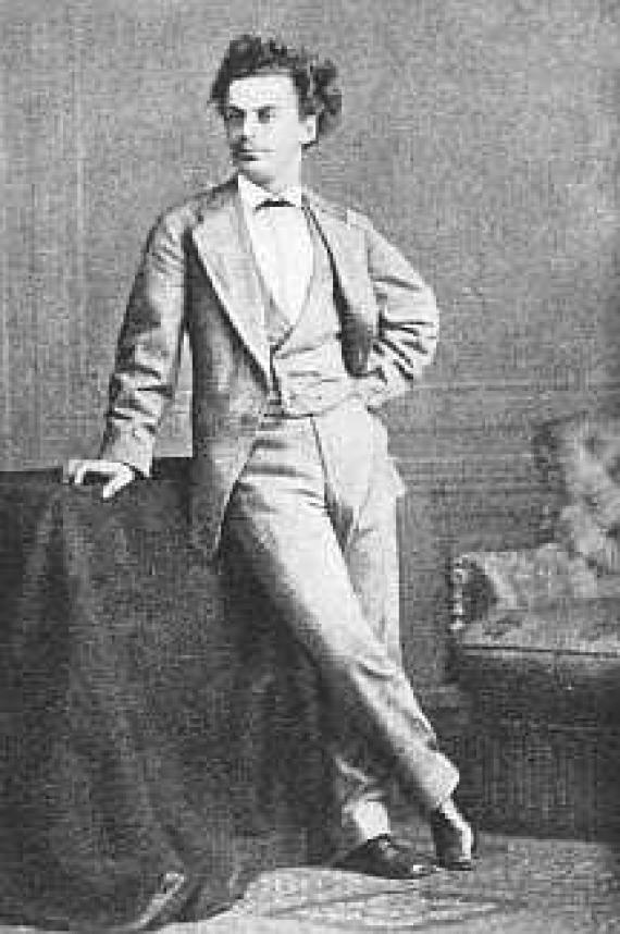 Black and white photograph of a young man in full figure leaning against a pedestal