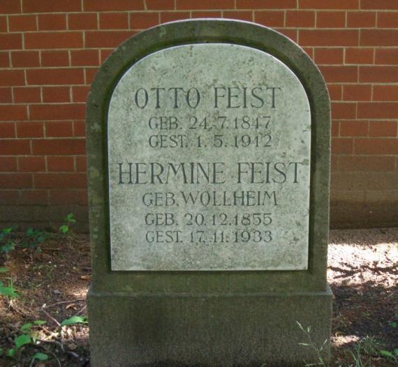 Color photograph of a gravestone in front of a red brick wall