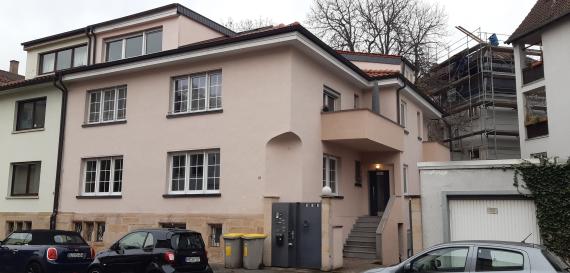 Mehrfamilienhaus mit Eingangstor und parkenden Autos entlang der Straße