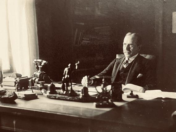 Black and white photograph of a man sitting at a desk with work materials on it