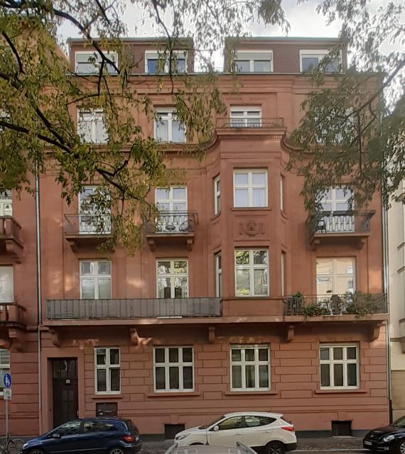 Apartment building with bay windows and balconies in a row of houses with parked cars in front