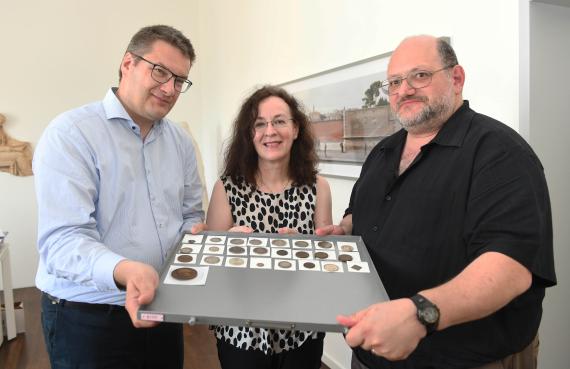 Three people presenting various coins and medals on a carrier plate