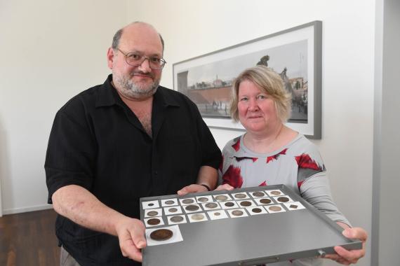 Zwei Personen, die eine Trägerplatte mit mehreren Münzen und Medaillen in Richtung Kamera präsentieren