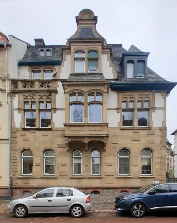 Farbfoto eines historischen Stadthauses mit parkenden Autos im Vordergrund