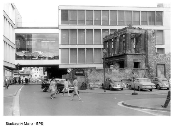 Black and white photo of a street with remains of an old residential building, modern building in the background, pedestrians on the street