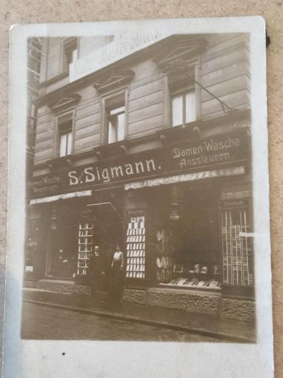 Historical photograph of a store with two people standing in front of it, looking towards the camera