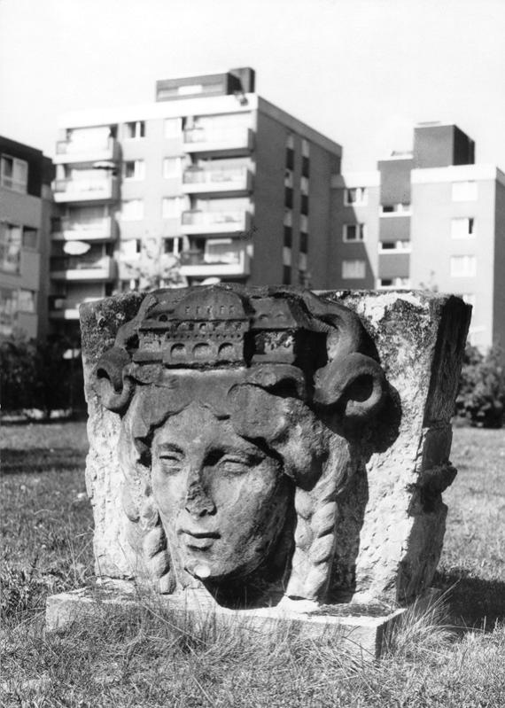 An ornamental stone with a woman's face, residential buildings in the background