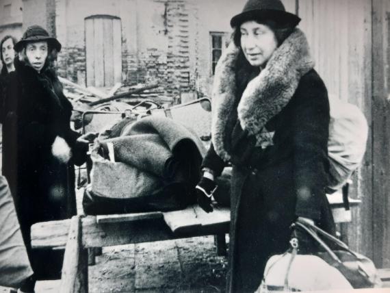 Black and white picture. In the foreground, a woman with a coat bearing the "Jewish star". In the background, other women and pieces of luggage.