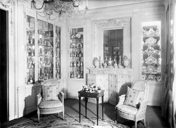 Black and white photograph of Hermine Feist's white-paneled showcase room. Dozens of porcelain objects can be seen in the recessed glass cabinets.