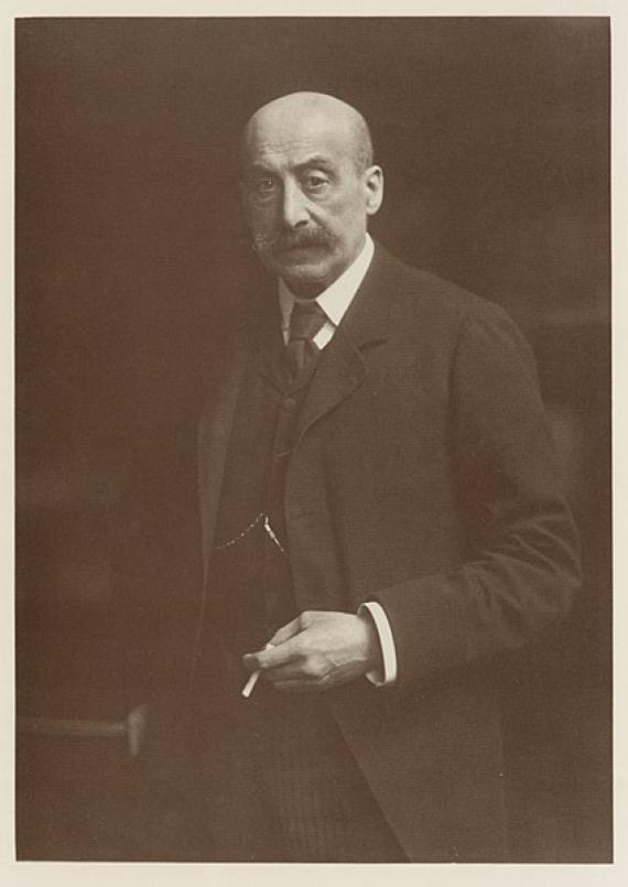 A black-and-white photograph shows Max Liebermann in a formal dark suit, with a visible watch chain and a cigarette in his hand