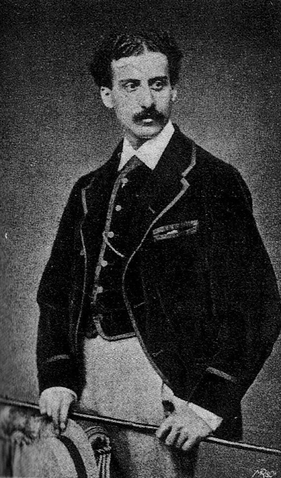 Black and white photograph of a standing young man wearing a three-piece leisure suit and a moustache.