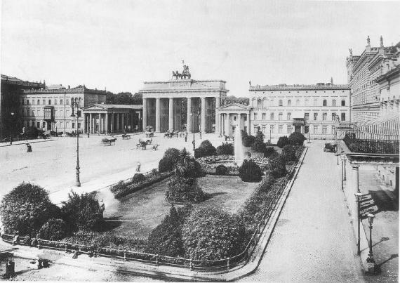 Eine zeitgenössische Schwarz-weiß-Fotografie zeigt das Brandenburger Tor in Berlin mit dem Palais Liebermann von einem erhöhten Betrachterstandpunkt aus