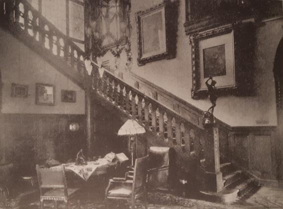 Historical image of an interior in a residential building, with an old staircase and large paintings on the wall