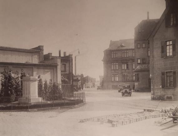 Historisches Bild auf eine Straße. Rechts und links einig Gebäude, und wenige Autos