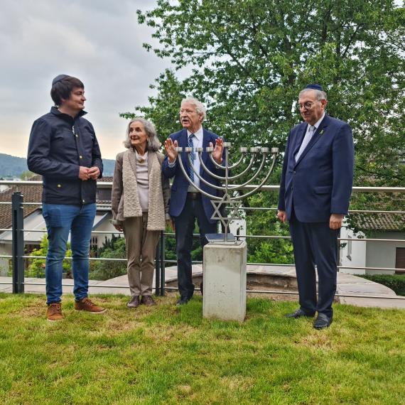 Abraham Lehrer, Roman Kovar, Marie Louise Jung und Bürgermeister Mario Dahm anlässlich der Enthüllung der Chanukkia im Mai 2024. Die Personen stehen um die  Chanukkia herum, die Chanukkia ist rund 140 cm hoch und steht auf einem Betonsockel.