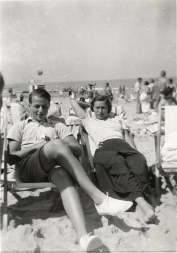 Schwarz-Weiß Bild. Ein junger Mann und seine Mutter, sitzend in Strandstühlen an einem Badestrand