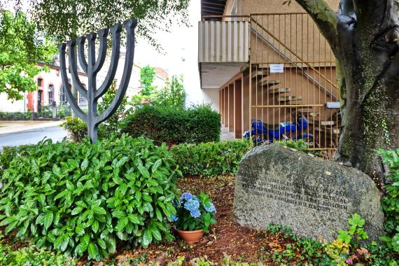 Under a tree on a street corner is a stone menorah and a memorial stone with the text: "The Poppelsdorf synagogue stood on this spot. It was built in 1902 and destroyed during the National Socialist violence against our citizens on November 9, 1938."