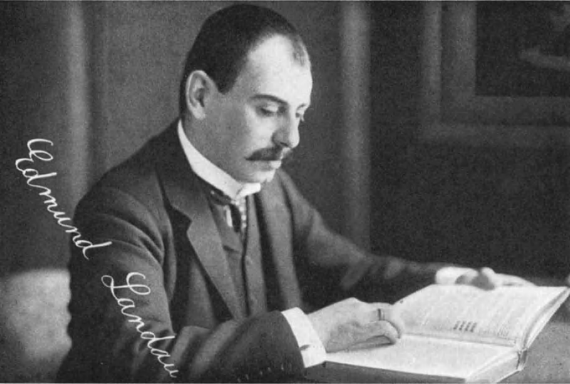 Das Bild zeigt den Mathematiker Edmund Landau in schwarz weiß. Er ist ein weißer einen Anzug tragender Mann mit Schnauzer und sitzt vor einem Buch, dem er seinen Blick widmet. Links in der Ecke des Fotos steht sein Name. 