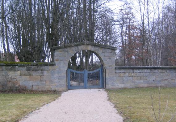 Mauerstein mit einem aus Metal Eingangstor, das in den Friedhof hineinführt