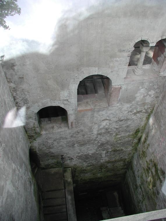 Blick von oben auf einen Schacht, auf der linken Seite eine kleine Treppe, die zum Badebecken führt