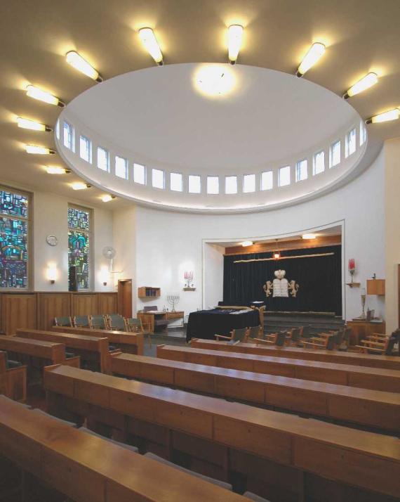 Interior of the synagogue with long wooden benches and a luminous ceiling