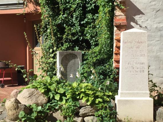 The gravestone on the left is estimated 1 meter high, made of dark stone, rectangular with a depression in the form of a round arch, which bears the epitaph ("Here rests in God our dearly beloved unforgotten husband, father and grandfather Commerzien-Rath Benjamin Engel" and date of birth and death). On the left is the larger gravestone for the married couple Helene and Wolf Salomon, made of light-colored stone with a simple inscription in Fraktur script (only names and dates of birth and death).