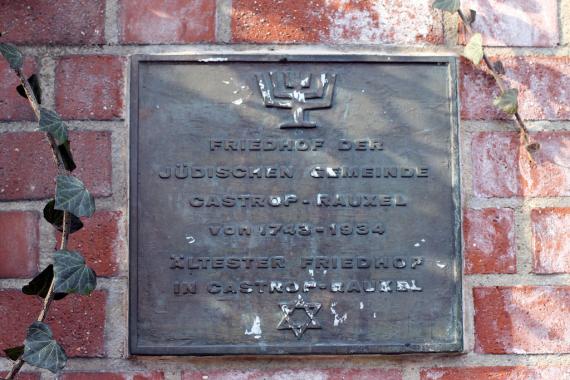 square commemorative metal plaque, in the head there is a menorah, then follows the text "Cemetery of the Jewish community Castrop-Rauxel from 1743 to 1934, oldest cemetery in Castrop-Rauxel" in the foot there is a Star of David.