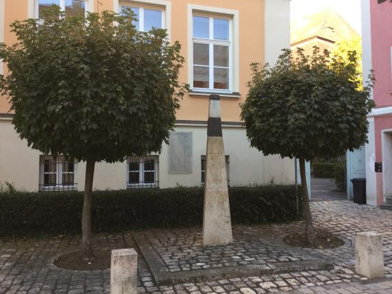 Gedenkstele auf einem Platz mit zwei kleinen Bäumen