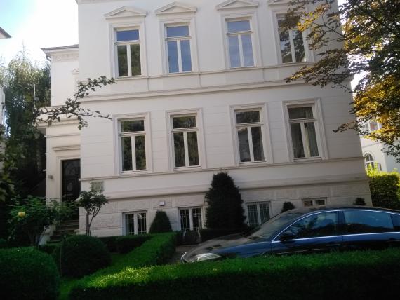 Front view of a white house with several rows of windows, right in front of it is a car.