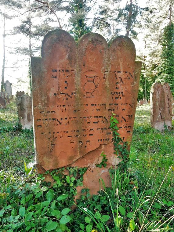 Grabstein eines Leviten, erkennbar an der Kanne. Grabstein aus rotem Sandstein. Im Fußbereich ist die Inschrift bereits durch Witterungseinflüsse zerstört.