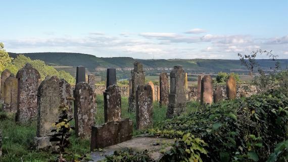 Jüdischer Verbandsfriedhof Laudenbach Jewish Union Cemetery Laudenbach. You can see a part of the cemetery with gravestones and outer wall. The view sweeps from the ridge far into the Main valley.