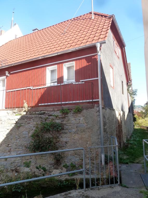 The house with the old house number 57 and 57 1/2, half-timbered house with red wooden boarding.  Under the building is a historic vaulted cellar. At the bottom of the picture flows the stream, secured with a railing.