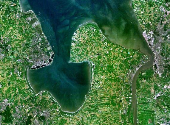 Bird's eye view of the Jade Bay, blue-green sea bay surrounded by green forests, the city of Wilhelmshaven and several small vacation villages, fields dominate the landscape